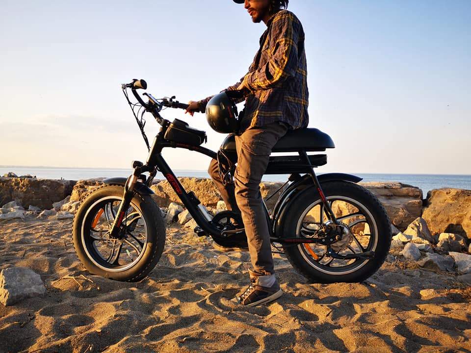 A man riding a DJ Super Bike fat tire e-bike on a sandy beach