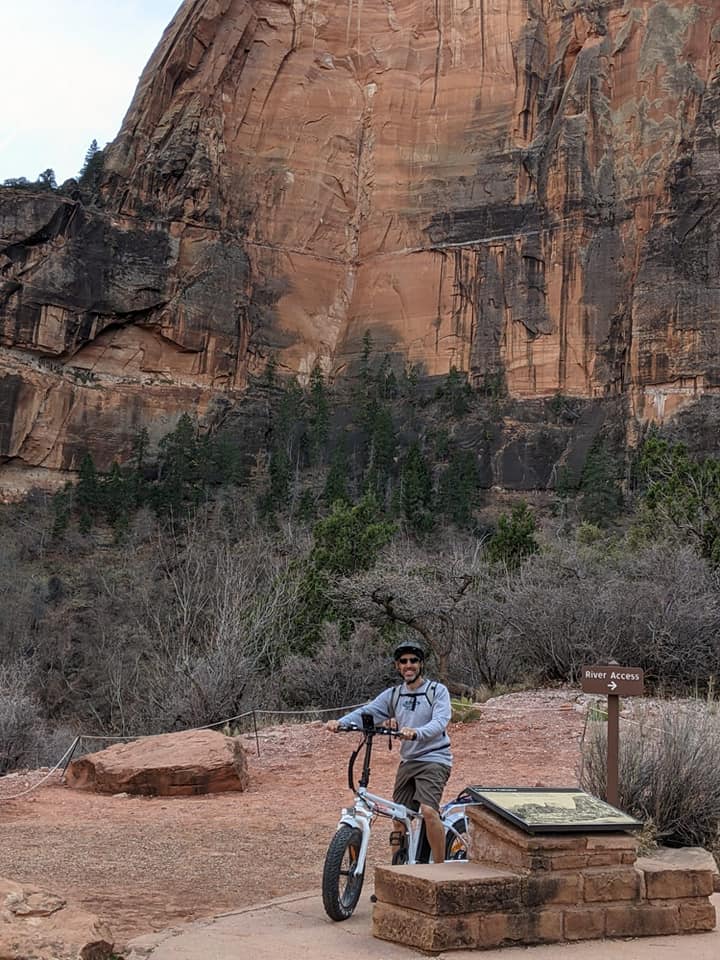 A smiling rider poses on a DJ Folding Bike fat tire e-bike in front of a rockface in Zion National Park