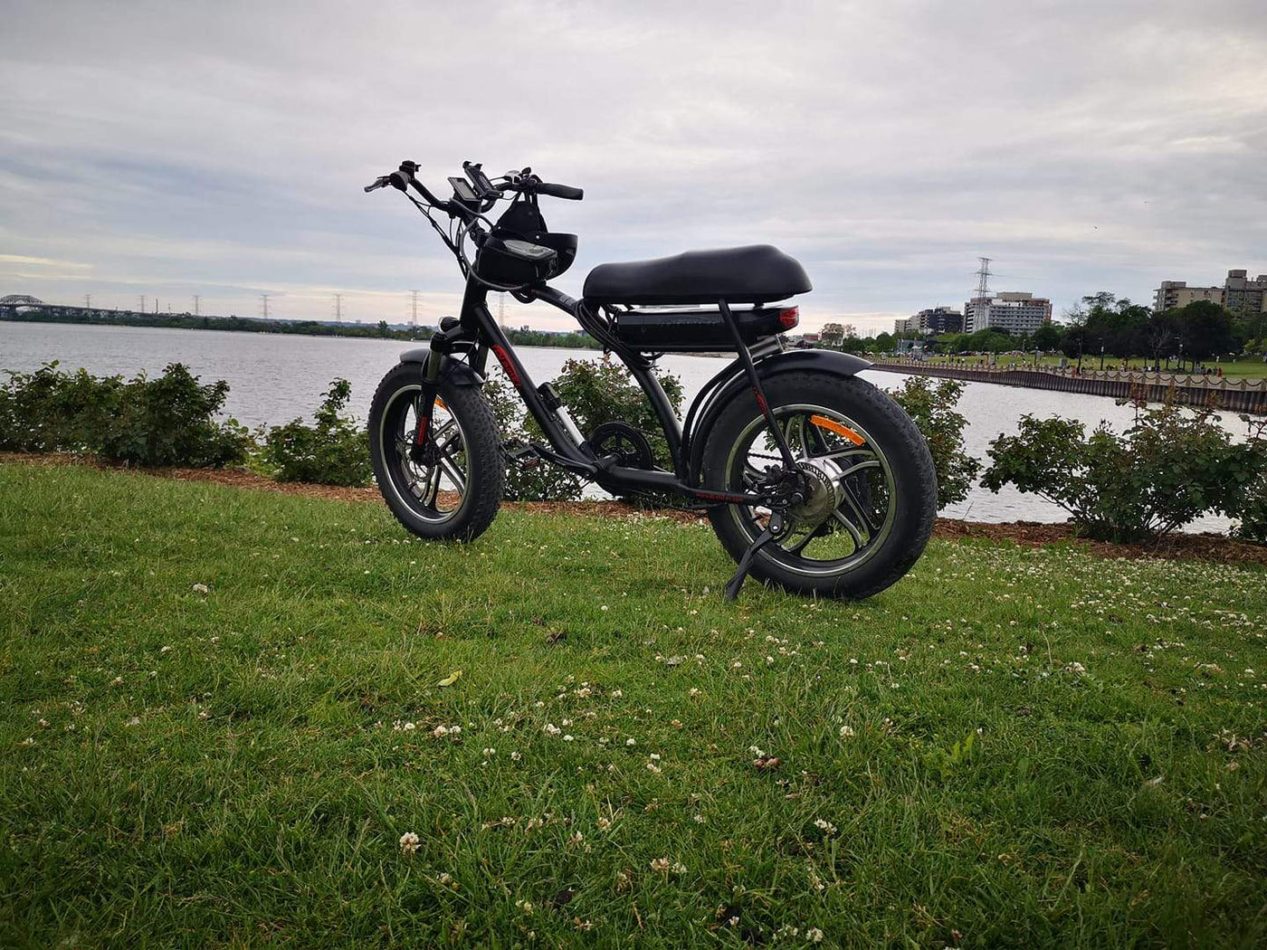 A DJ Super Bike fat tire e-bike equipped with cell phone holder on the grass in front of a lake in Burlington, Ontario